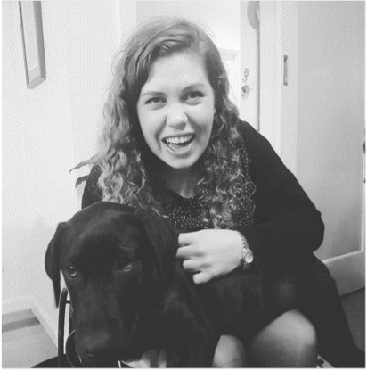 Black and white photo of a female wheelchair user with curly hair. She is holding a Labrador and laughing.