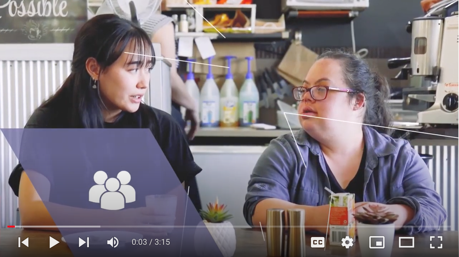 Screenshot of the video featuring two women sitting in a coffee shop with a computer