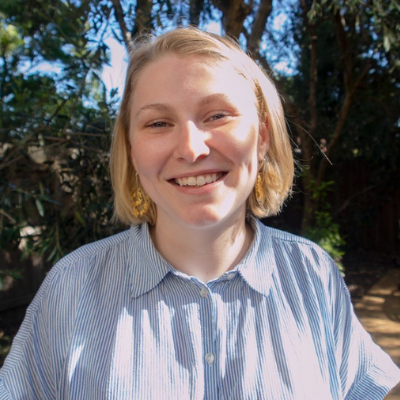 A smiling woman with short blonde hair and a pinstriped shirt, outdoors in a park.