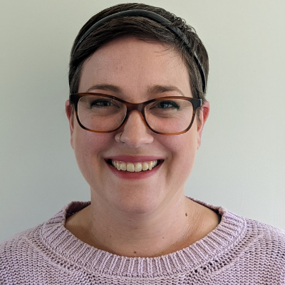 A woman with short dark hair, glasses and a purple knit jumper.