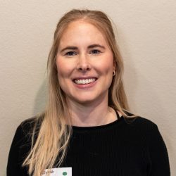 Photo of Elysia wearing a black jumper and her blond hair down, smiling at the camera.