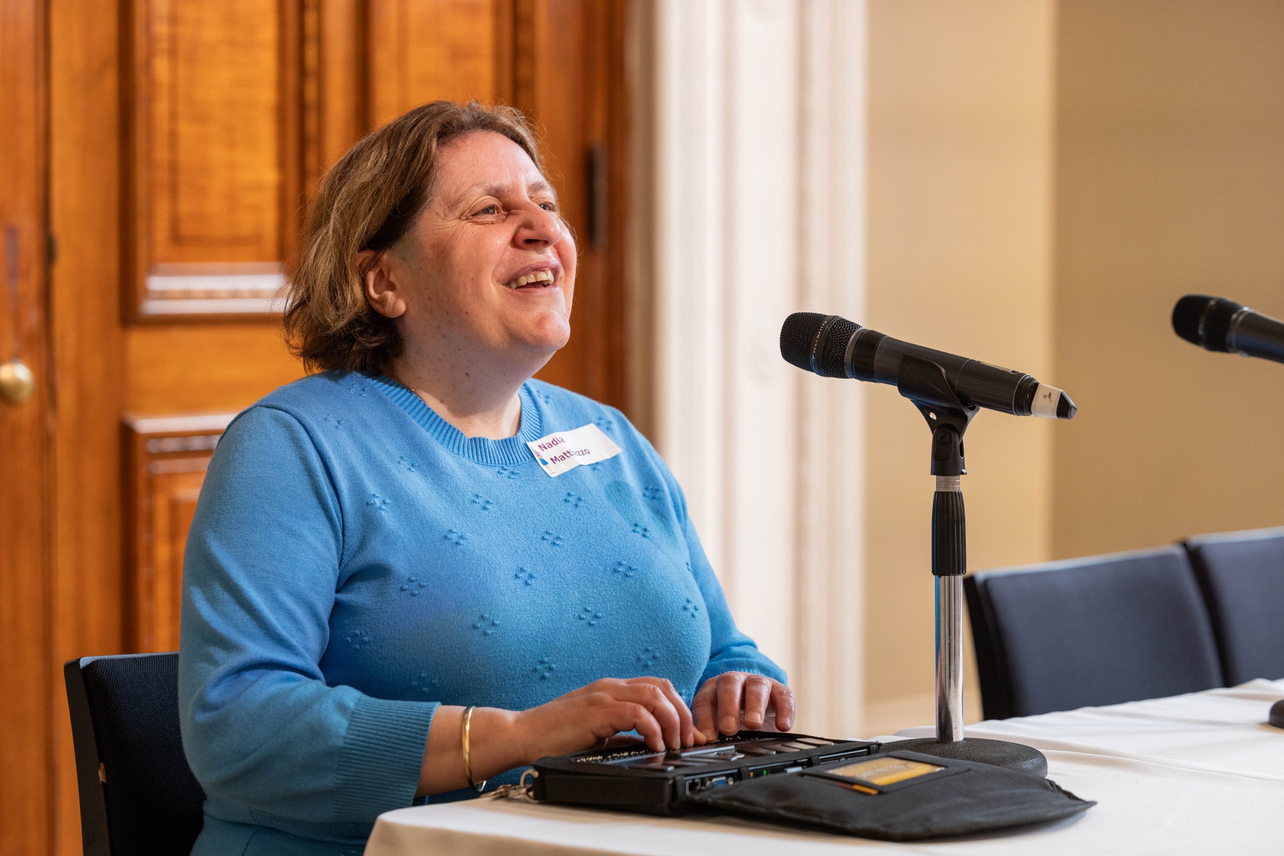 CEO Nadia Mattiazzo speaks into the microphone smiling and using her braille reader