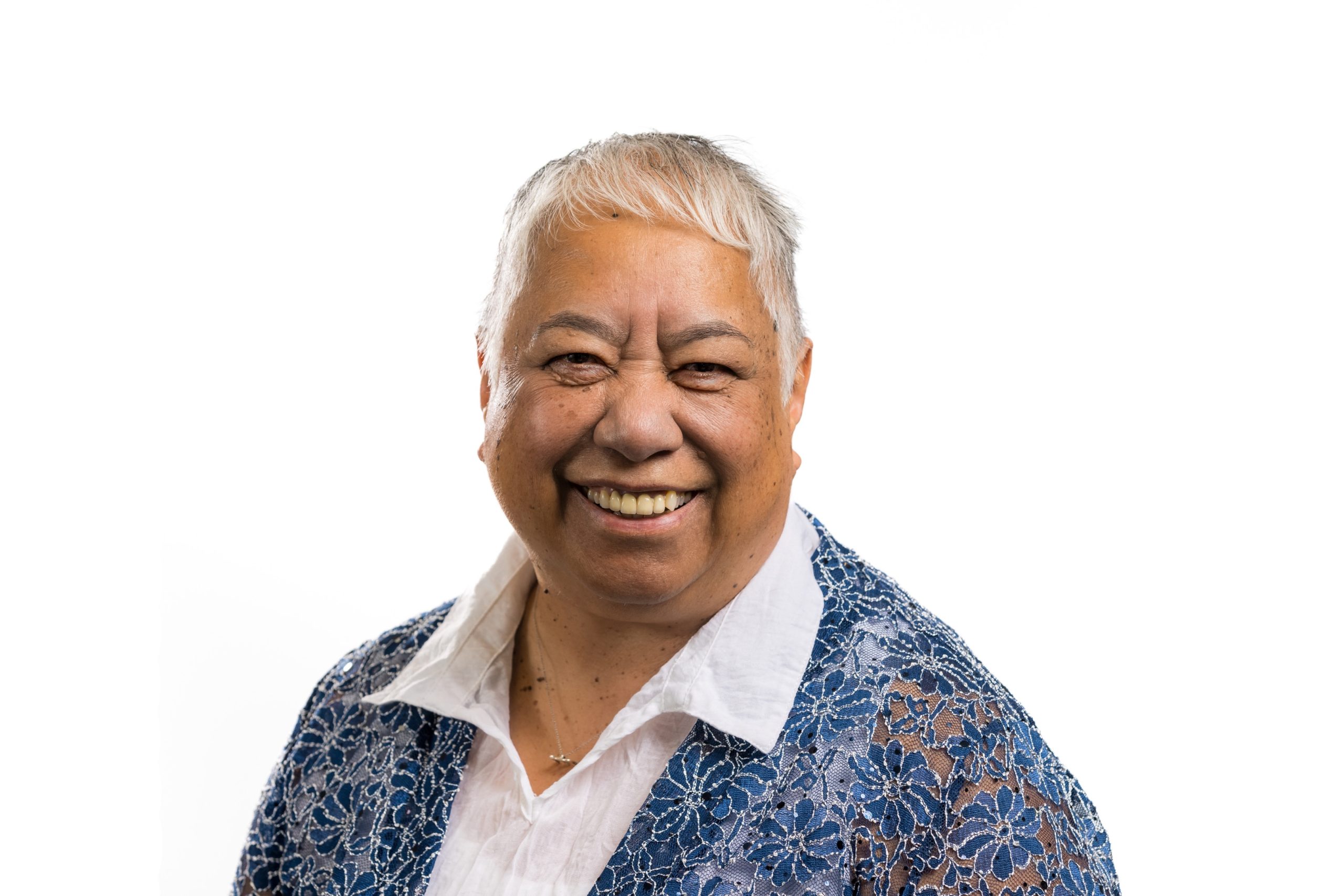 Board member Maggie Toko. Maggie is smiling at the camera and wearing a white shirt with a blue patterned cardigan.