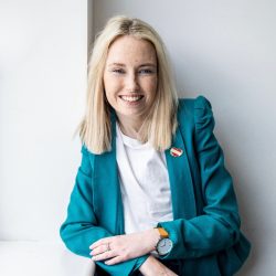 Photo of Stephanie Sayer, smiling and facing the camera. Stephanie is wearing a blue blazer.